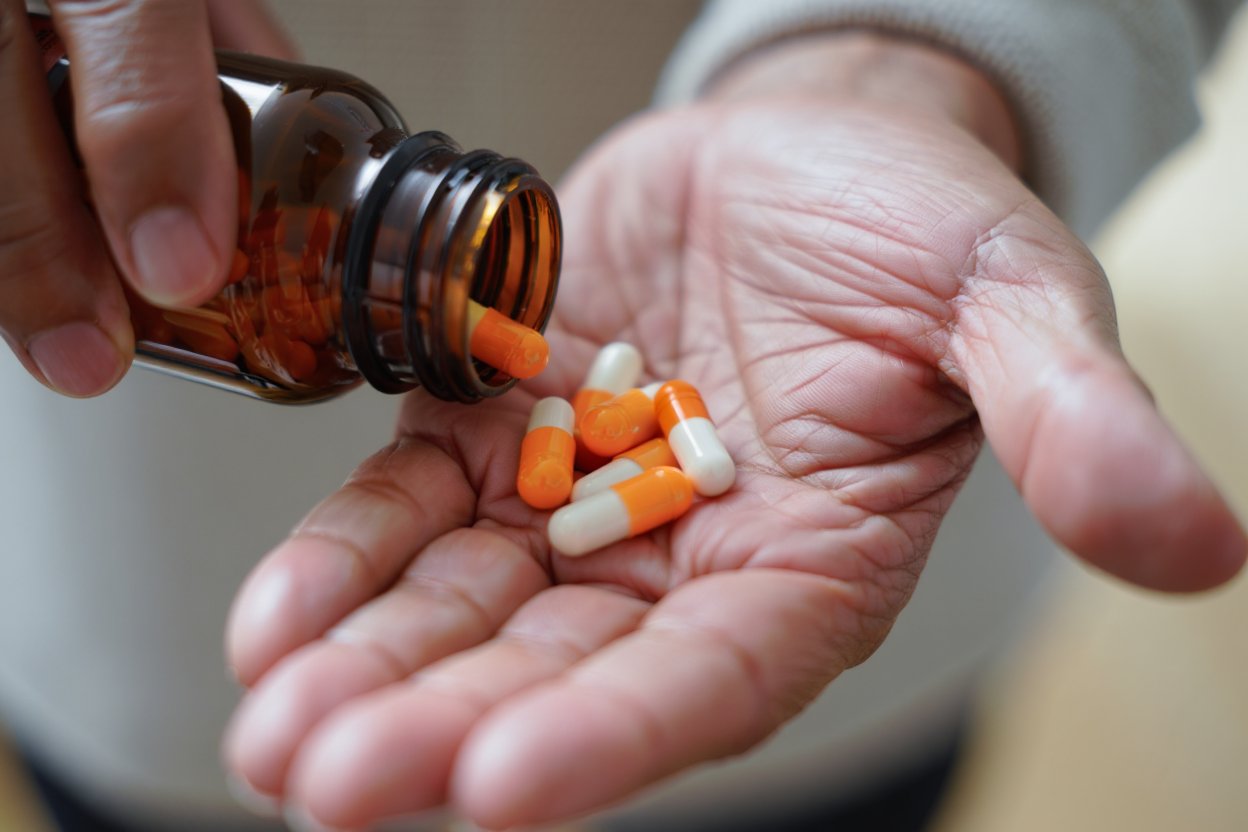 Оранжево-белые капсулы высыпаются из флакона на ладонь — признак необходимости лечения лекарственной зависимости.